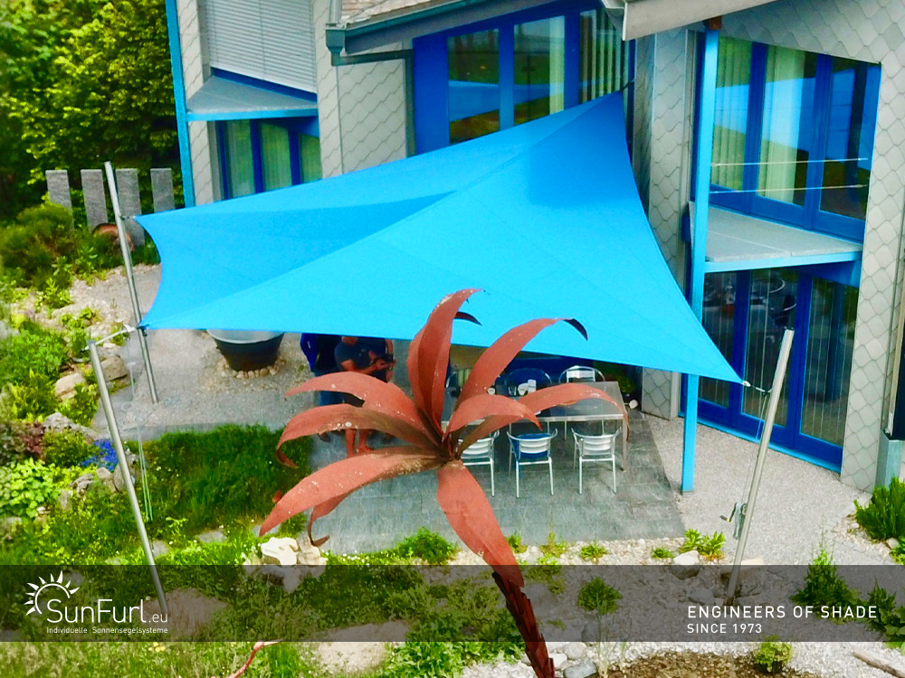 Blaues SunFurl Sonnensegel mit drei Pfosten und einer Wandhalterung