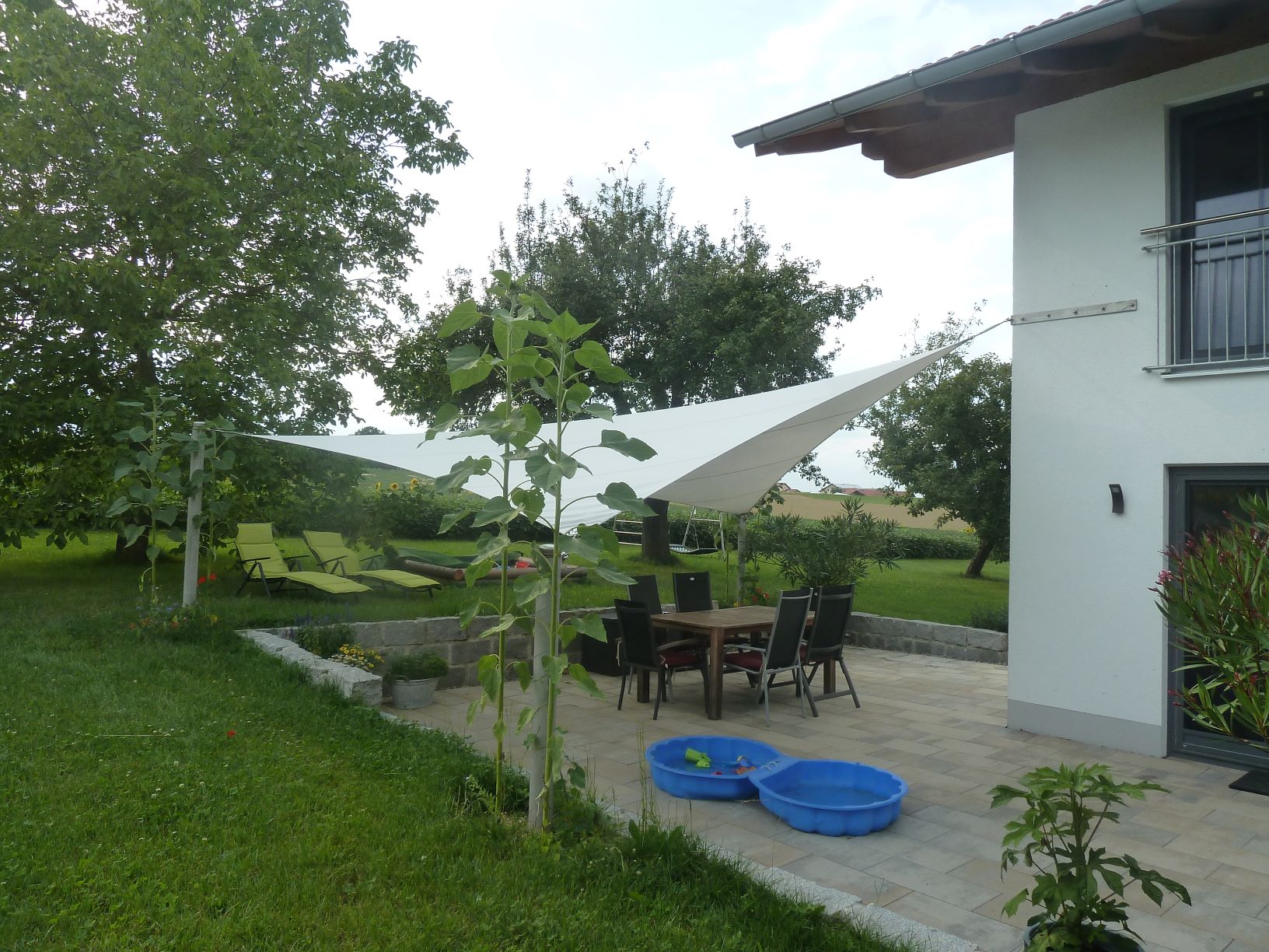3D-Strahlensegel-2 weißes Strahlensegel mit Montage an Außenecke am Haus und drei Pfosten im Garten über Terrasse