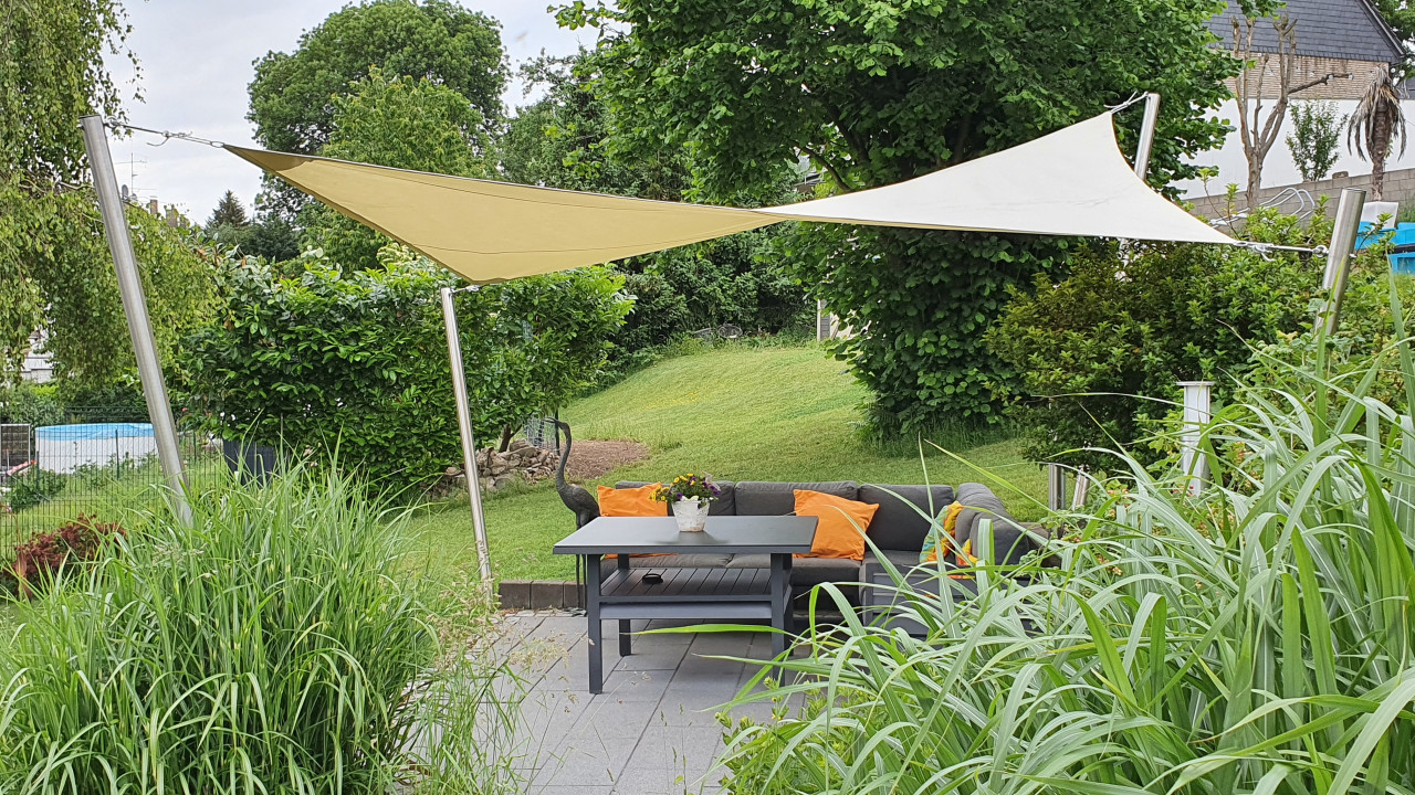 3D Sonnensegel über Sitzgruppe dreidimensionales, beiges Sonnensegel an vier Pfosen im Garten über einer Terrasse mit Sitzgruppe