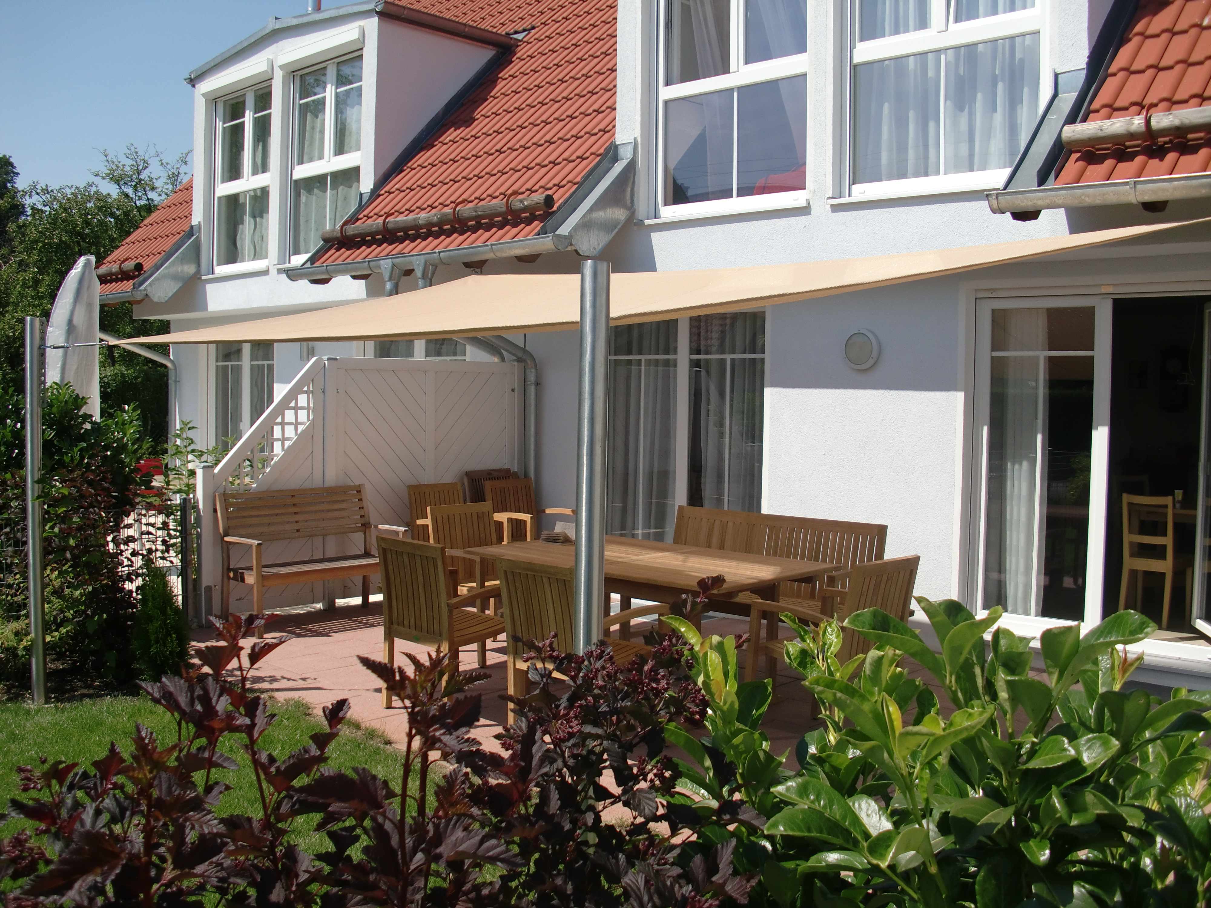 beiges Viereck Sonnensegel mit Befestigungen am Haus und zwei Pfosten über einer Terrasse